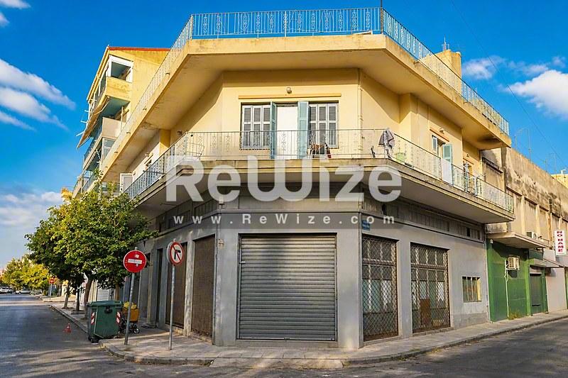 Γωνιακό οικόπεδο με πρόσοψη μεζονέτας στη Χαλκιδική, κίτρινο κτίριο πολλών επιπέδων με εμπορικό χώρο στο ισόγειο.