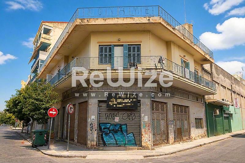Γωνιακή όψη μεζονέτας στη Χαλκιδική με κίτρινες τοίχους, μπλε παντζούρια και εμπορικό χώρο στο ισόγειο.