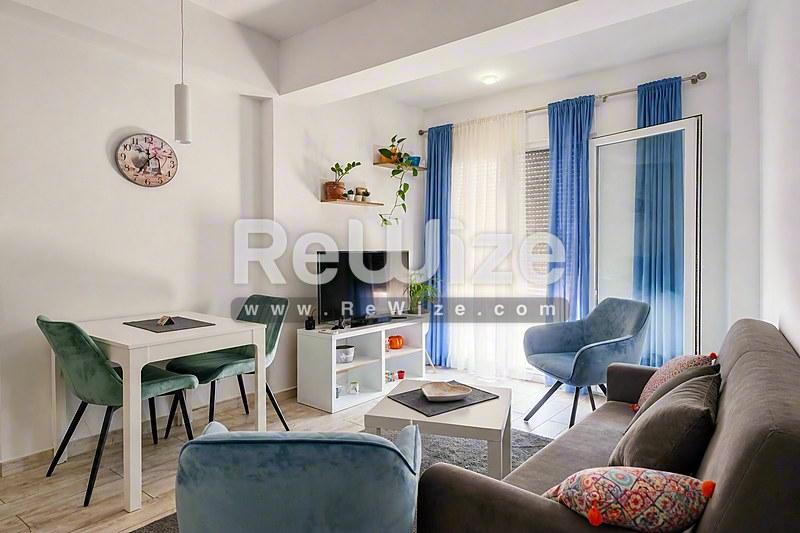 Φωτεινό σαλόνι διαμερίσματος στη Χαλκιδική με άνετη συνθέσεις και γαλάζιες κουρτίνες.