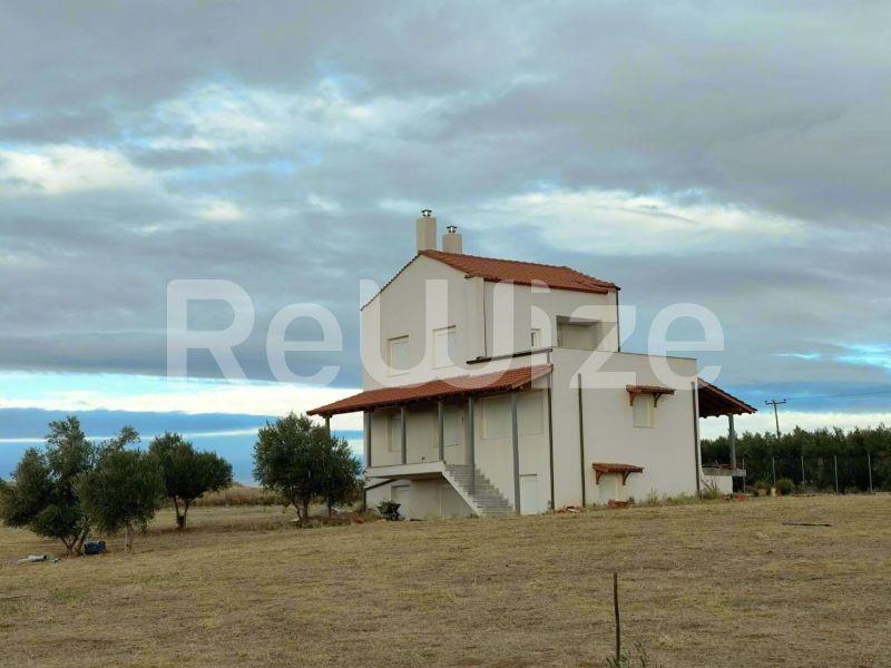 Πρόσοψη μονοκατοικίας με κόκκινη στέγη στην Χαλκιδική, με κρεμ χρώμα τοίχων και αγροτικό περιβάλλον.