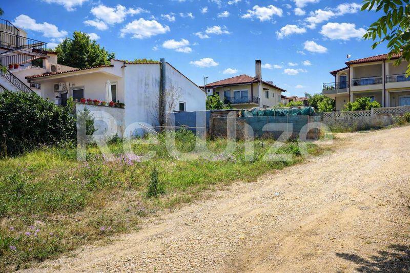 Οικόπεδο προς κατασκευή στη Χαλκιδική με γειτονικές κατοικίες και δασώδη περιοχή.
