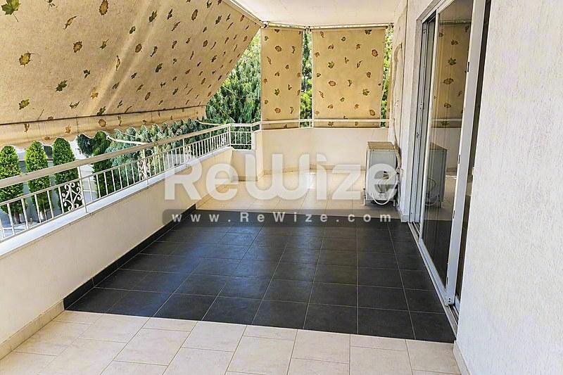 Ευρύχωρη σκεπαστή βεράντα διαμερίσματος στη Χαλκιδική με σκούρο δάπεδο και πανοραμική θέα στη θάλασσα.