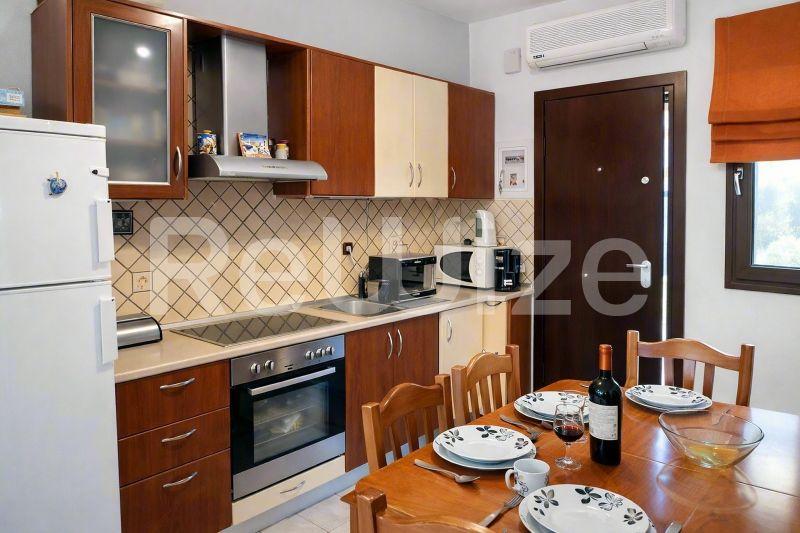Σύγχρονη κουζίνα μεζονέτας στη Χαλκιδική με ξύλινα ντουλάπια, ενσωματωμένο φούρνο και τραπέζι φαγητού.
