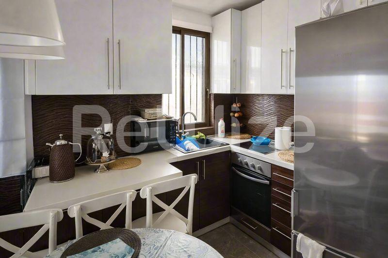 Σύγχρονη κουζίνα μεζονέτας στη Χαλκιδική με λευκά ντουλάπια, σκούρες κάτω μονάδες και ανοξείδωτες συσκευές.