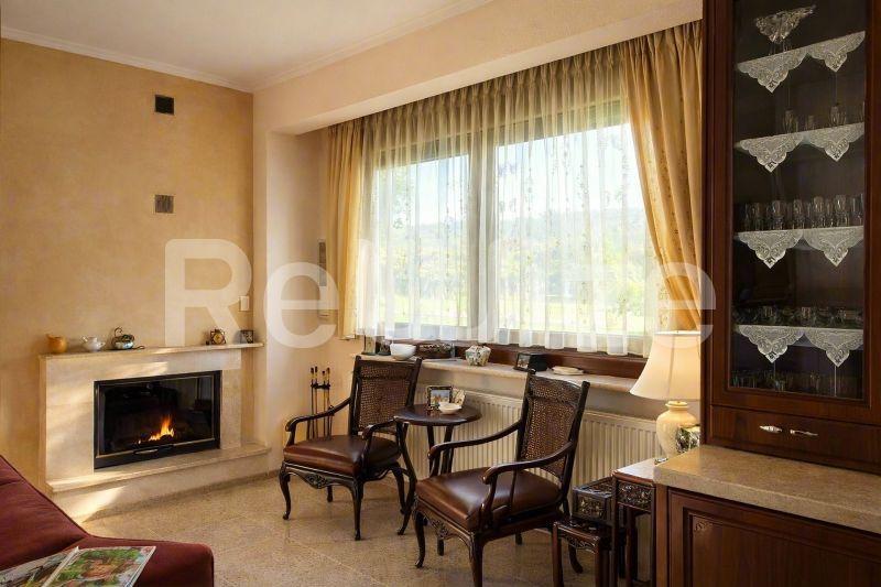 Κομψό σαλόνι της βίλας στην Χαλκιδική με τζάκι, ξύλινα έπιπλα και μεγάλα παράθυρα με χρυσές κουρτίνες.