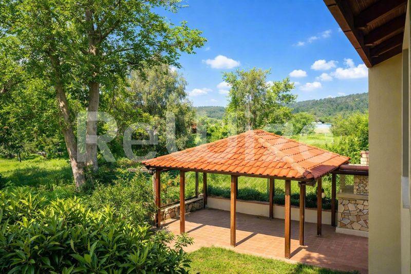 Ξύλινη περγόλα με κεραμοσκεπή σε μονοκατοικία στη Χαλκιδική, με θέα σε πράσινους κήπους και βουνά.