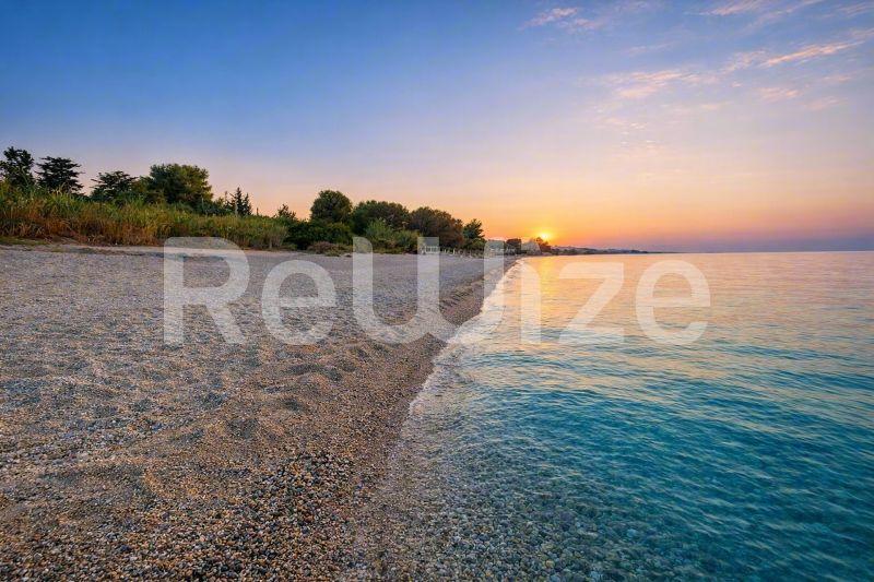 Εκπληκτική θέα ηλιοβασιλέματος στην παραλία από μονοκατοικία στη Χαλκιδική με χρυσή άμμο και γαλάζια νερά.