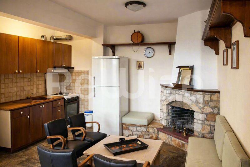 Άνετη κουζίνα και χώρος διαβίωσης μονοκατοικίας στη Χαλκιδική με ξύλινα ντουλάπια και τζάκι.
