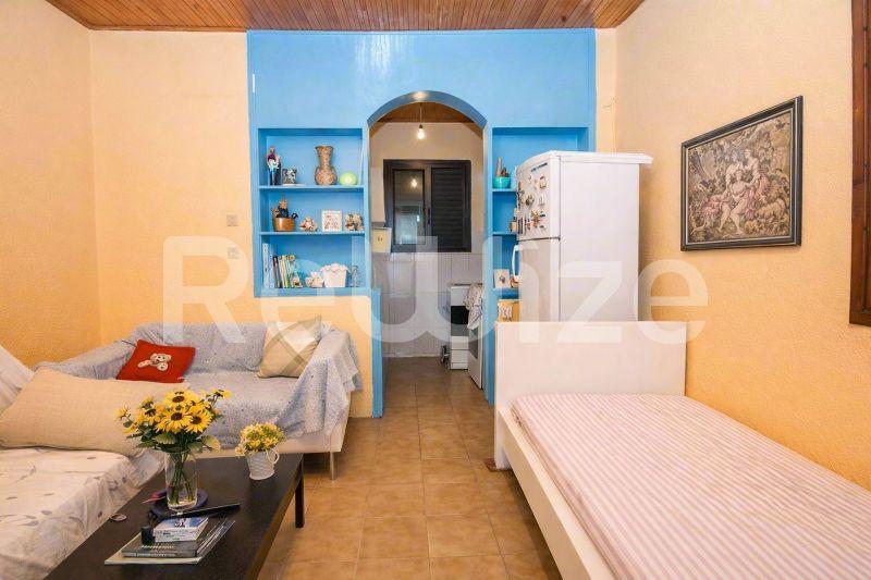 Φωτεινό σαλόνι μιας μονοκατοικίας στη Χαλκιδική, Σιθωνία, με καναπέ, κρεβάτι, μπλε ράφια και σύγχρονη κουζινέτα.