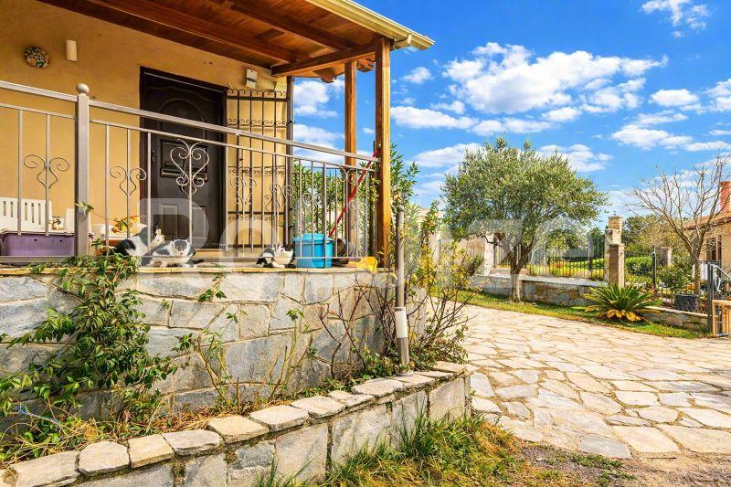 Πρόσοψη μονοκατοικίας στη Χαλκιδική με πέτρινη βάση, κίτρινα τοιχώματα και σκεπαστή βεράντα.