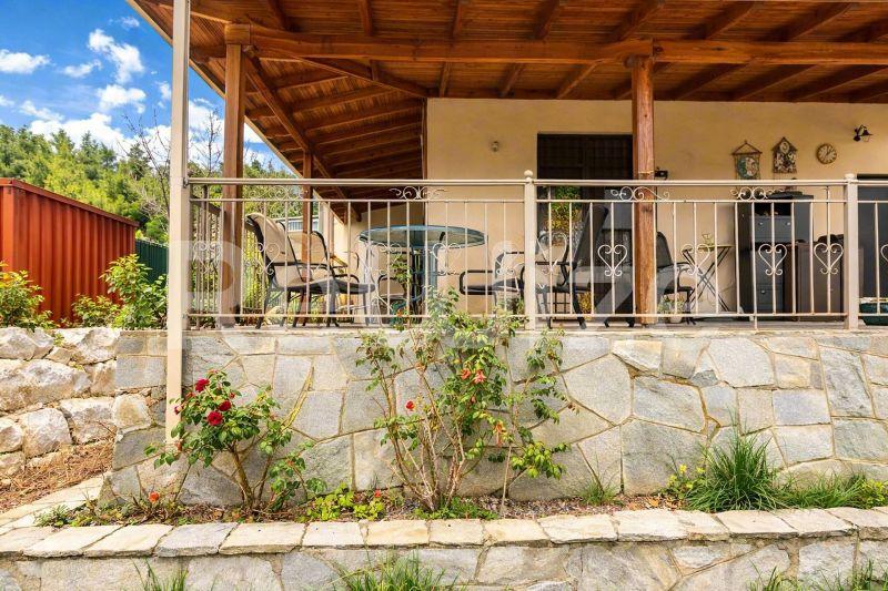 Просторна terasa od kamena detached house-a u Halkidiki-ju sa udobnim sedištem i bujnom zelenilom ispod drvene pergole.