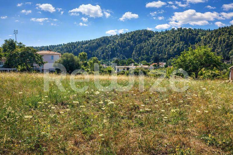 Просторο γήπεδο στη Χαλκιδική με πράσινη βλάστηση, δασώδη λόφια και σπίτια στο βάθος.