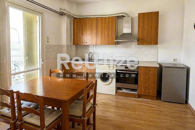 Φωτεινή κουζίνα με ξύλινα ντουλάπια, τραπέζι και σύγχρονες συσκευές στο διαμέρισμα της Χαλκιδικής.
