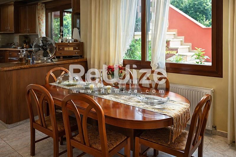 Κομψό τραπεζαρία με ξύλινο τραπέζι και καρέκλες σε μονοκατοικία στη Χαλκιδική, με μεγάλα παράθυρα με θέα στον κήπο.
