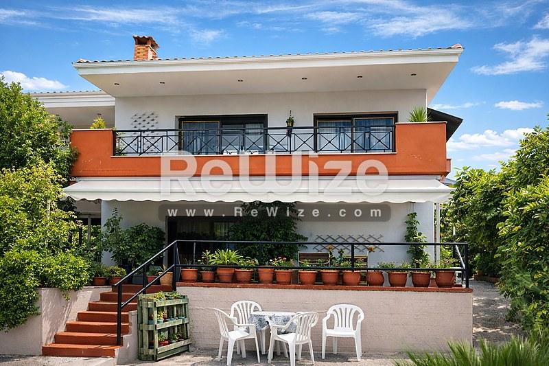 Σύγχρονη αρχιτεκτονική όψη μονοκατοικίας στη Χαλκιδική με πορτοκαλί στοιχεία και βεράντα.