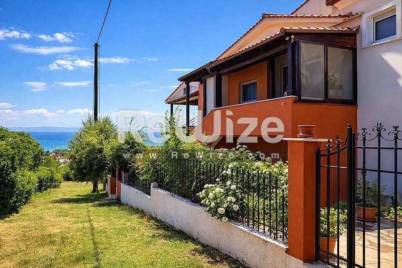 Όμορφη μονοκατοικία στη Χαλκιδική με πορτοκαλί-τερακότα πρόσοψη, θέα θάλασσας και πράσινους κήπους.
