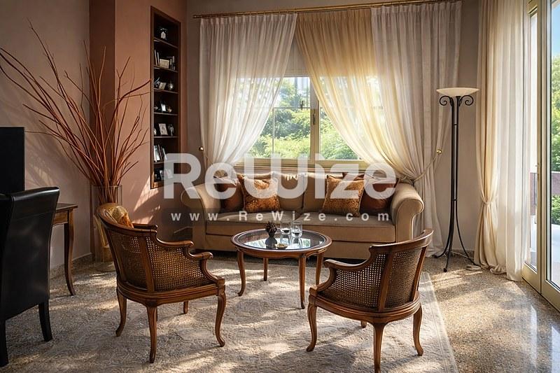 Κομψό σαλόνι σε μονοκατοικία στη Χαλκιδική με καφέ καναπέ, πολυθρόνες και πανοραμικά παράθυρα με διαφανή κουρτίνες.