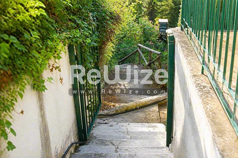 Είσοδος μεζονέτας στη Χαλκιδική με στενή πέτρινη σκάλα ανάμεσα σε λευκά τοιχώματα και πράσινες πύλες.
