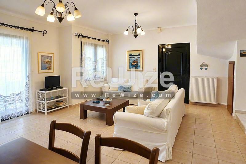 Φωτεινό σαλόνι μεζονέτας στη Χαλκιδική με κρεμ έπιπλα, ξύλινες δοκούς και κομψό πάτωμα πλακιδίων.