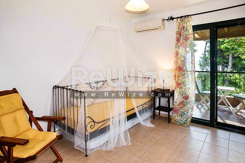 Φωτεινό σαλόνι μεζονέτας στη Χαλκιδική με κρεβάτι με σκούρο και κίτρινη πολυθρόνα.