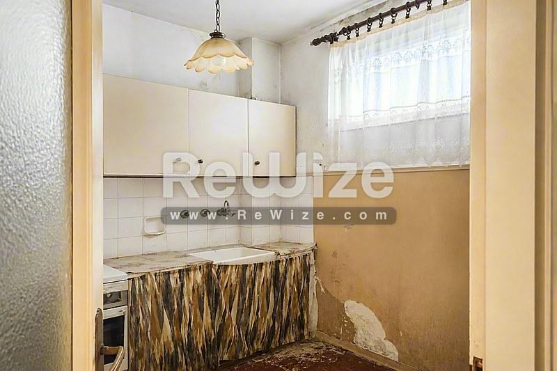 Μικρή κουζίνα σε διαμέρισμα στη Χαλκιδική με λευκά ντουλάπια, βασικές συσκευές και μικρό παράθυρο.