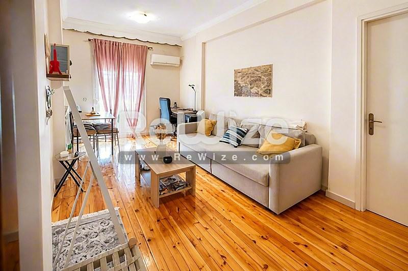Φωτεινό σαλόνι διαμερίσματος στη Χαλκιδική με ξύλινα πατώματα, άνετο καναπέ και μεγάλα παράθυρα.