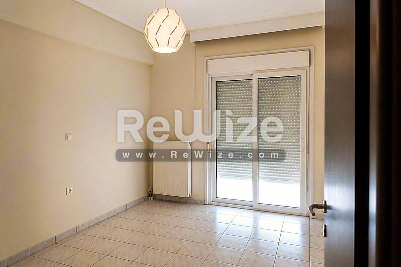 Φωτεινό υπνοδωμάτιο διαμερίσματος στη Χαλκιδική με σύγχρονο δάπεδο, ουδέτερα χρώματα και γυάλινες πόρτες.