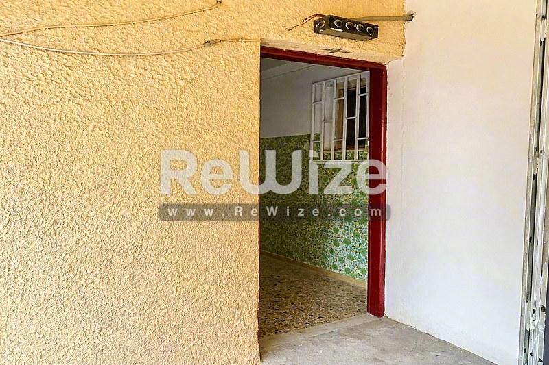 Είσοδος διαμερίσματος στη Χαλκιδική με κόκκινη θυρόπλακα και κίτρινα υφαντά τοιχώματα.