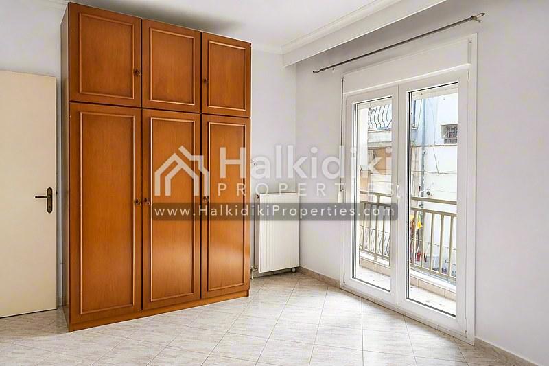 Φωτεινό υπνοδωμάτιο σε διαμέρισμα στη Χαλκιδική με ξύλινες ντουλάπες και πρόσβαση στο μπαλκόνι.