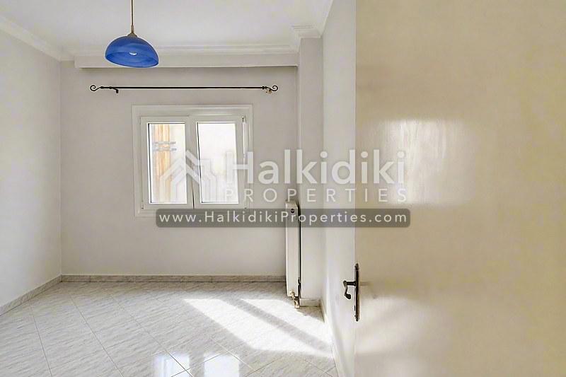 Φωτεινό υπνοδωμάτιο διαμερίσματος στη Χαλκιδική με μπλε κρεμαστό φωτιστικό και φυσικό φως.