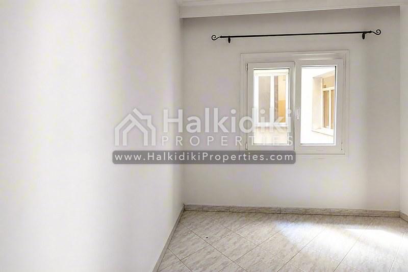 Φωτεινό υπνοδωμάτιο σε διαμέρισμα στη Χαλκιδική με λευκούς τοίχους, ξύλινο δάπεδο και μεγάλο παράθυρο.