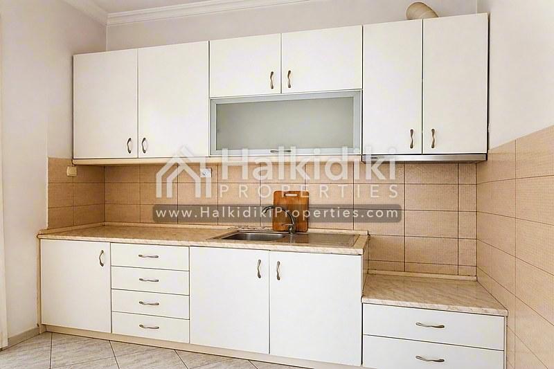 Συμπαγή κουζίνα διαμερίσματος στη Χαλκιδική με λευκά ντουλάπια και καφέ πλακάκια backsplash.