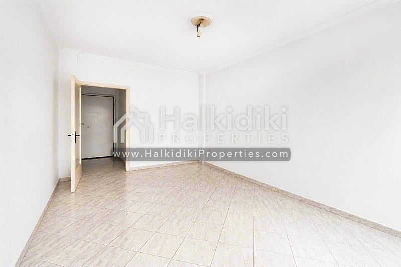Φωτεινό σαλόνι διαμερίσματος στη Χαλκιδική με ανοιχτό ξύλινο δάπεδο και καθαρά λευκά τοιχώματα.