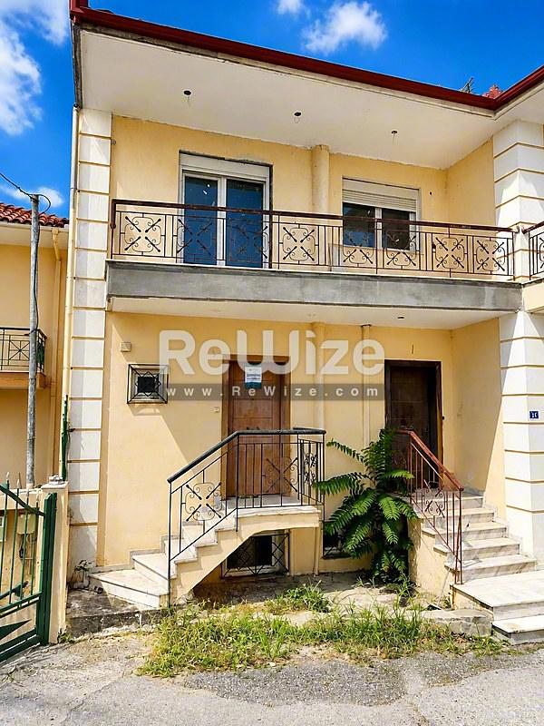 Κίτρινη πρόσοψη σύγχρονης μεζονέτας στη Χαλκιδική με μπλε παντζούρια και σιδερένια μπαλκόνια.