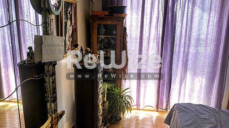 Υπνοδωμάτιο στο ακίνητο Halkidiki rw-7568 με μωβ κουρτίνες, φυτά και ξύλινα έπιπλα.