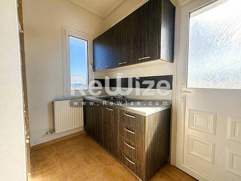 Σύγχρονη κουζινέτα στο διαμέρισμα Halkidiki rw-7586 με σκούρα ντουλάπια και συμπαγή χώρο εργασίας.