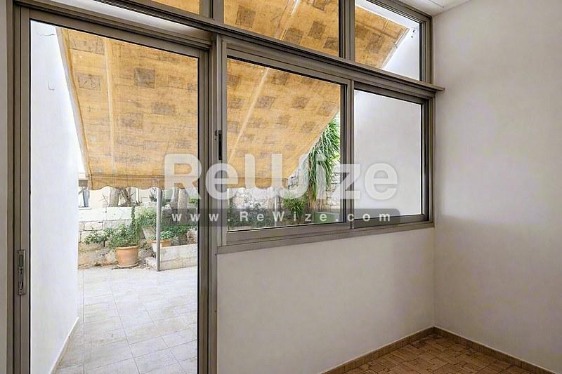 Φωτεινό σαλόνι σε διαμέρισμα της Χαλκιδικής με γυάλινες πόρτες που ανοίγουν σε ηλιόλουστο μπαλκόνι και φυσικές υφαντές σκιάδες.