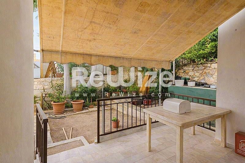 Ευρύχωρη βεράντα του rw-7603 στη Χαλκιδική με σκιασμένη ζώνη καθιστικού, φυτά σε γλάστρες και ξύλινα έπιπλα.